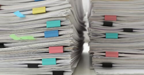 Stacks of documents with paper clips on office desk, closeup